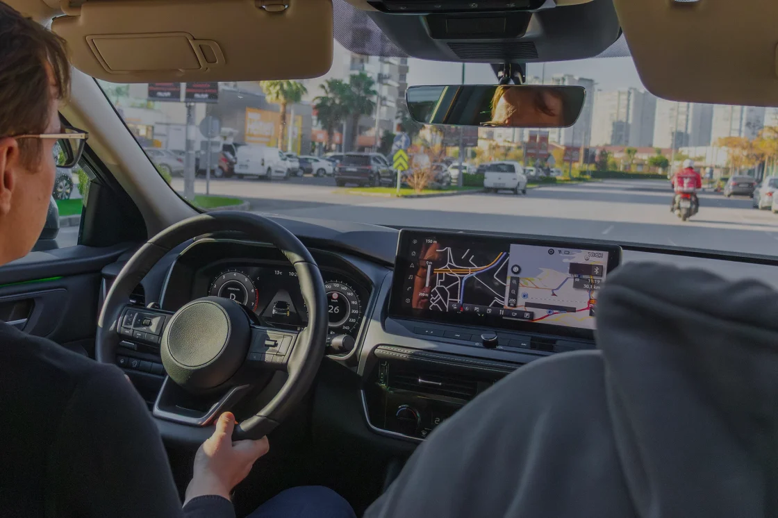 Mann fährt im Auto, Blick geht über seine Schulter und raus durch die Windschutzscheibe